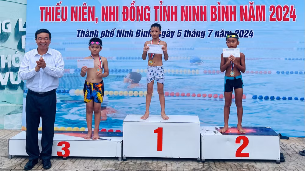 Ban tổ chức trao giải cho các vận động viên nam nội dung 25 m bơi ếch lứa tuổi 6-8.