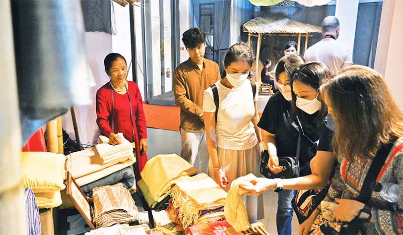 Du khách nước ngoài tham quan, tìm hiểu các sản phẩm lụa tại triển lãm Trưng bày giới thiệu nghề ươm tơ, dệt vải truyền thống vùng đồng bằng Bắc Bộ. Ảnh: DUY ĐĂNG