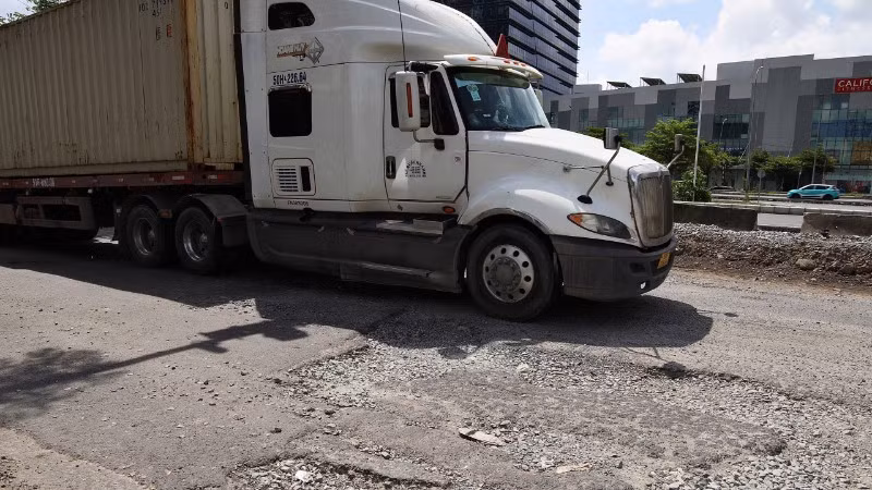 Xe tải lưu thông khó khăn giữa vòng vây ổ voi, ổ gà trên tuyến đường Nguyễn Văn Linh. (Ảnh: QUÝ HIỀN)