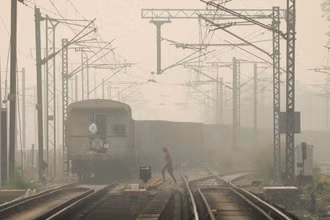 Một người phụ nữ băng qua đường ray khi tàu chở hàng chạy qua, vào một ngày sương mù ở New Delhi, Ấn Độ. Ảnh chụp ngày 12/11/2021. Ảnh: Reuters.