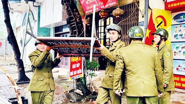 Lực lượng chức năng xã Nam Phù xử lý các biển hiệu quảng cáo lấn chiếm vỉa hè. (Ảnh NGHIÊM XUYÊN)