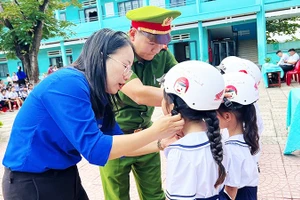 Giáo viên và cán bộ Công an hướng dẫn học sinh đội mũ bảo hiểm đúng cách.