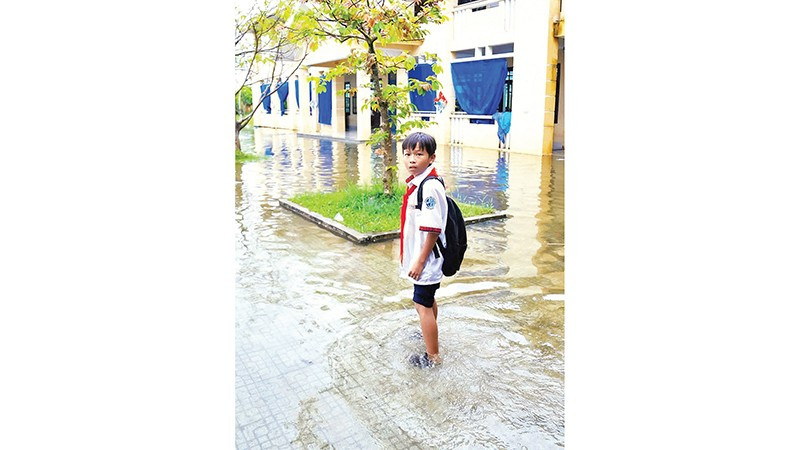 Mỗi khi trời mưa, nước dâng ngập đường, học sinh phải đi vòng, vào đến cổng trường lại phải lội nước trong sân để vào lớp. (Ảnh QUỐC CƯỜNG)
