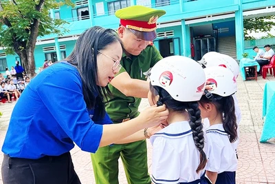 Giáo viên và cán bộ Công an hướng dẫn học sinh đội mũ bảo hiểm đúng cách.