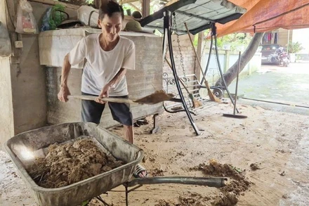 Ông Bùi Văn Nghiếp, tổ dân phố Sơn Hải thu dọn bùn đất còn đọng lại trên sân nhà. (Ảnh: TRỊNH LAN)