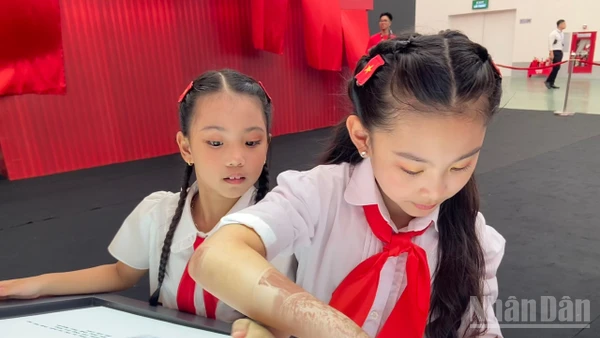 Em Đỗ Phương Linh cùng bạn khám phá sách tương tác mapping tại Triển lãm “95 năm Cờ Đảng soi đường”.