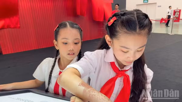 Em Đỗ Phương Linh cùng bạn khám phá sách tương tác mapping tại Triển lãm “95 năm Cờ Đảng soi đường”.