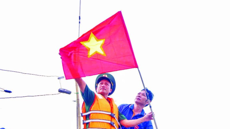 Cán bộ, chiến sĩ Đồn Biên phòng cửa khẩu cảng Thuận An tuyên truyền và tặng cờ Tổ quốc cho ngư dân vươn khơi, bám biển. (Ảnh VÕ TIẾN)