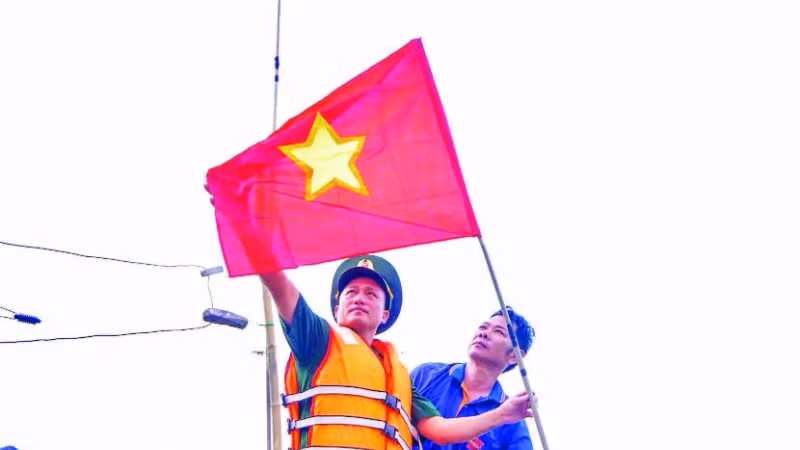 Cán bộ, chiến sĩ Đồn Biên phòng cửa khẩu cảng Thuận An tuyên truyền và tặng cờ Tổ quốc cho ngư dân vươn khơi, bám biển. (Ảnh VÕ TIẾN)