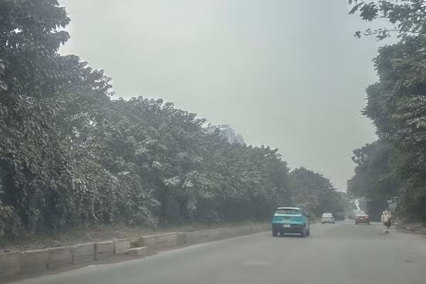 Tuyến đường gom Đại lộ Thăng Long (đoạn qua khu vực gần Thiên Đường Bảo Sơn) chìm trong lớp bụi dày đặc, mịt mù. Cây cối ven đường đổi sang màu trắng đục, phủ đầy lớp bột mịn. (Ảnh: THÙY LINH)
