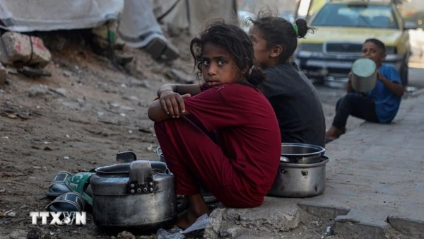 Trẻ em ngồi chờ nhận thức ăn cứu trợ ở thành phố Gaza. (Ảnh: THX/TTXVN)
