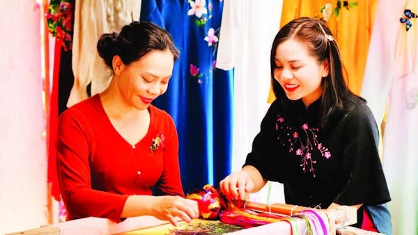 Nghệ nhân Nguyễn Thị Hằng (bên trái) giới thiệu kỹ thuật thêu trên lụa. (Ảnh: THÀNH NAM)