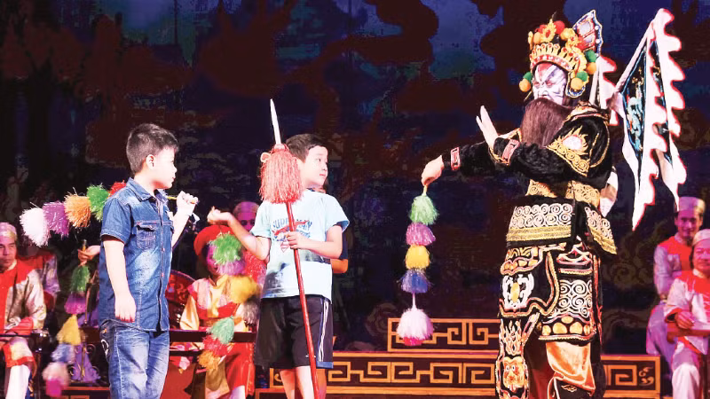 Các bạn nhỏ Câu lạc bộ Đọc sách cùng con trải nghiệm đạo cụ tuồng trên sân khấu. (Ảnh: Câu lạc bộ Đọc sách cùng con)