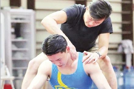 Huấn luyện viên Trương Minh Sang hỗ trợ vận động viên phục hồi sau buổi tập của đội tuyển thể dục dụng cụ quốc gia. (Ảnh NV)