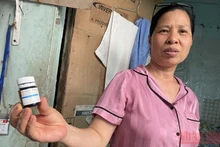Bà Mai Thị Hường cùng lọ thuốc canxi dạng viên dùng tạm thay thế trong khi hết thuốc. (Ảnh: SƠN BÁCH)
