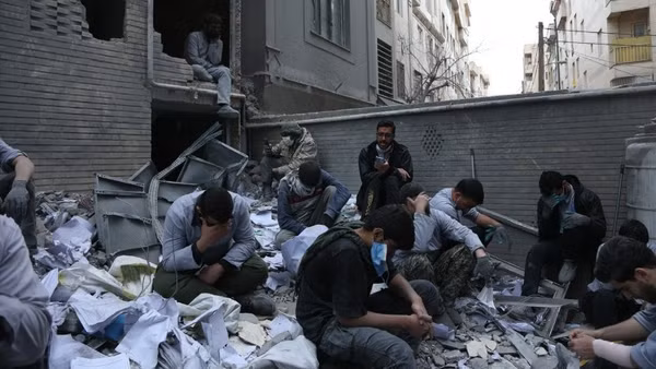 Người dân Iran bên những toà nhà đổ nát sau các cuộc không kích của Mỹ và Israel xuống thủ đô Tehran ngày 15/3/2026. (Ảnh: THX/TTXVN)