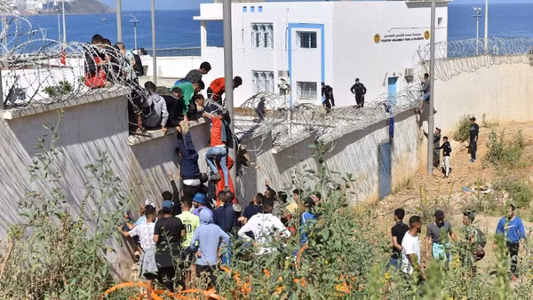 Người di cư trèo qua hàng rào biên giới để vào vùng lãnh thổ Ceuta của Tây Ban Nha từ thành phố Fnideq, Maroc. (Ảnh: THX/TTXVN)