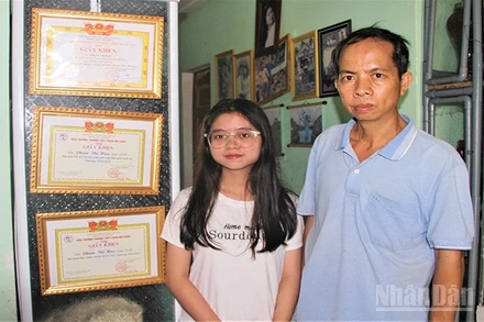 Em Phạm Thị Hậu và cậu ruột Ngô Thanh Đoàn đứng bên các thành tích học của em Hậu.