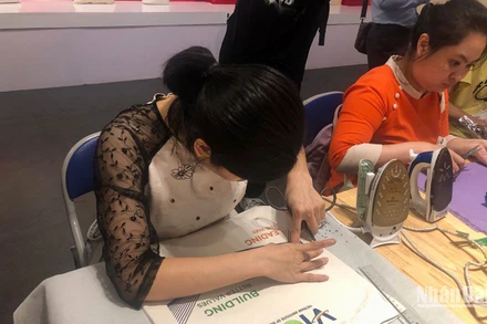 Một thợ thủ công của Vụn Art đang trổ các họa tiết trang trí bằng lụa trên túi vải với đầu mũi kéo.