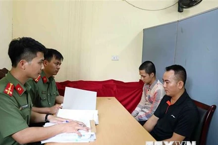 Lực lượng chức năng lấy lời khai bị can Nguyễn Quang D. (áo đen) và bị can Đinh Tiến S. (áo kẻ). (Ảnh: Phạm Kiên/TTXVN)