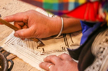 Nghệ nhân người H’Mông vẽ sáp ong trên vải lanh.(Ảnh: Hà Nam)