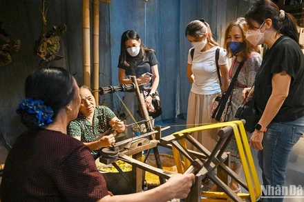 Du khách nước ngoài tìm hiểu về nghề ươm tơ, dệt vải truyền thống tại triển lãm “Muôn nẻo đường tơ”. (Ảnh DUY ĐĂNG)