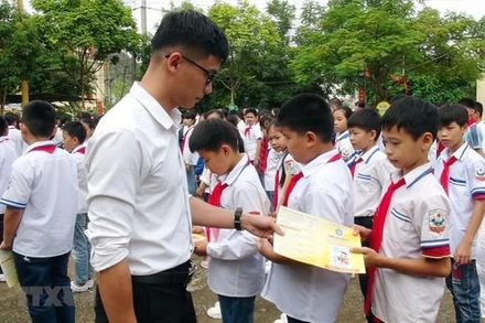 Cán bộ bảo hiểm phát tờ rơi tuyên truyền về bảo hiểm y tế học sinh. (Ảnh: TTXVN)