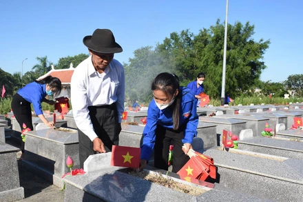 Ông Nguyễn Bá Sanh hướng dẫn các em đoàn viên thanh niên của xã Hòa Phong cắm cờ Tổ quốc lên phần mộ từng liệt sĩ.