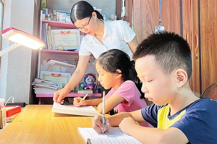 Mẹ đỡ đầu (Hội Phụ nữ phường An Phụ, thị xã Kinh Môn) hướng dẫn hai chị em Lương Thị Thanh Hiền và Lương Việt Hoàng làm bài tập. 