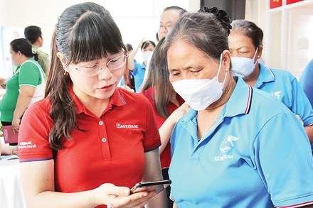 Nhân viên Agribank Chi nhánh Nhà Bè hướng dẫn người dân huyện Nhà Bè (Thành phố Hồ Chí Minh) thao tác thanh toán không dùng tiền mặt. (Ảnh Thế Anh)