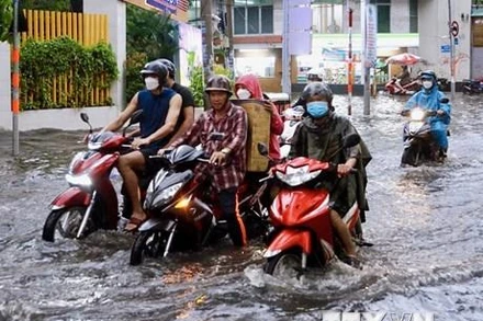 Người dân vất vả di chuyển trên đoạn ngập sâu ở đường Quốc Hương (thành phố Thủ Đức). (Ảnh: Hồng Giang/TTXVN)