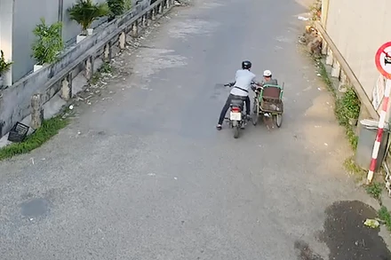 Trần Thanh Vũ (ngồi mô-tô) giả vờ hỏi mua rồi cướp 96 tờ vé số của ông Nguyễn Văn Vĩnh đang ngồi xe lăn. (Ảnh từ camera an ninh).