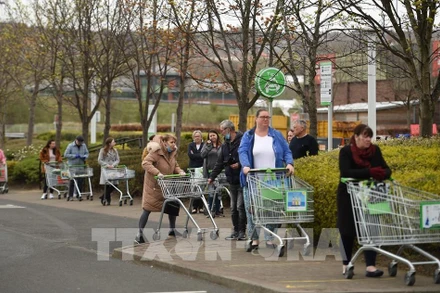 Người dân thực hiện giãn cách xã hội phòng lây nhiễm Covid-19 khi xếp hàng chờ mua sắm bên ngoài 1 siêu thị ở Gateshead, Anh, ngày 9/4/2020. (Ảnh: AFP/TTXVN)