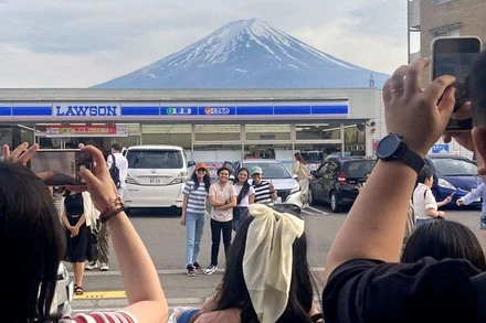 Khách du lịch chụp ảnh với khung cảnh núi Phú Sĩ phía sau cửa hàng tiện lợi Lawson ở thị trấn Fujikawaguchiko, tỉnh Yamanashi, Nhật Bản, ngày 28/4/2024. (Ảnh: Reuters/Kyodo) 