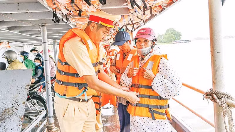 Cảnh sát đường thủy Công an thành phố Cần Thơ hướng dẫn người dân mặc áo phao đúng cách, bảo đảm an toàn mùa mưa lũ. (Ảnh DUY LINH)