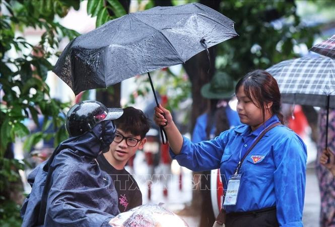 Tình nguyện viên hỗ trợ đón thí sinh vào điểm thi trong cơn mưa sáng 9/1 (Ảnh: TUẤN ANH/TTXVN)
