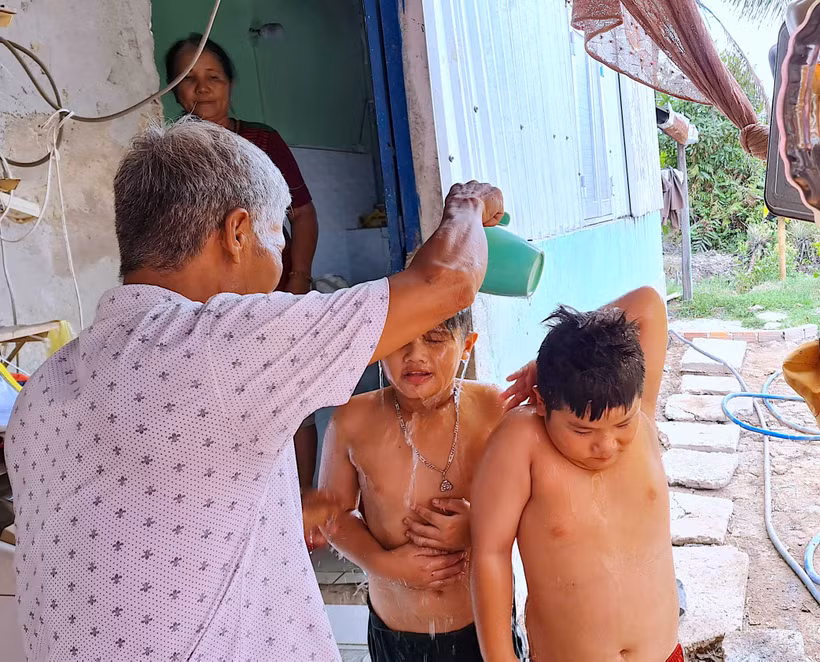 Bé Tuấn Khải, Tuấn Quy (ấp Minh Hà B) được người nhà dội rửa lại bằng ít nước ngọt sau khi tắm nước mặn dưới vuông tôm.