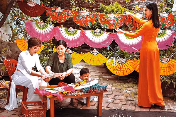 Bà Nguyễn Thị Tuấn (thứ hai, từ trái sang) giới thiệu cách làm quạt với du khách.