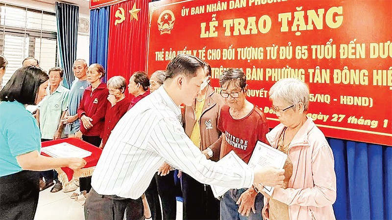 Trao thẻ Bảo hiểm y tế cho người cao tuổi phường Tân Đông Hiệp. (Ảnh: VÕ LÊ)