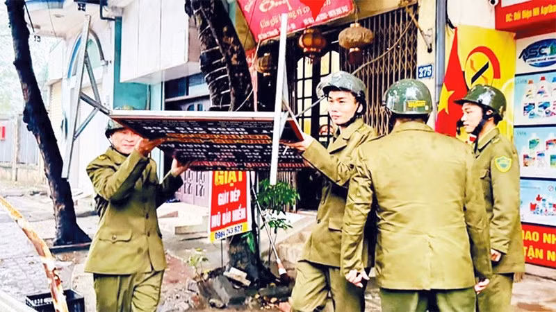Lực lượng chức năng xã Nam Phù xử lý các biển hiệu quảng cáo lấn chiếm vỉa hè. (Ảnh NGHIÊM XUYÊN)