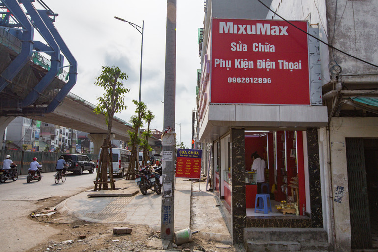 Cửa hàng phụ kiện điện thoại của anh Thế Thành nằm trên mặt đường Minh Khai. Do giải phóng mặt bằng nên hiện chưa có địa chỉ, số nhà cụ thể. Anh Thành mới kinh doanh được 4 tháng, lúc thuê thì mặt bằng đã nhỏ như hiện tại, rộng 2m, mặt tiền gần 8m. Nhà siêu mỏng trên đường vành đai 2 -0
