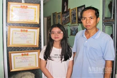 Em Phạm Thị Hậu và cậu ruột Ngô Thanh Đoàn đứng bên các thành tích học của em Hậu.