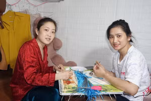 Chị Trang (bên phải) và chị Xiêm nỗ lực làm tranh cuốn giấy, vừa để kiếm thêm tiền trang trải chi phí, vừa để quên đi phần nào bệnh tật.