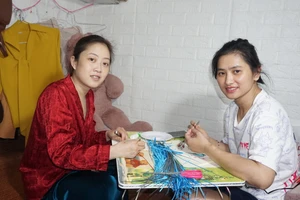 Chị Trang (bên phải) và chị Xiêm nỗ lực làm tranh cuốn giấy, vừa để kiếm thêm tiền trang trải chi phí, vừa để quên đi phần nào bệnh tật.