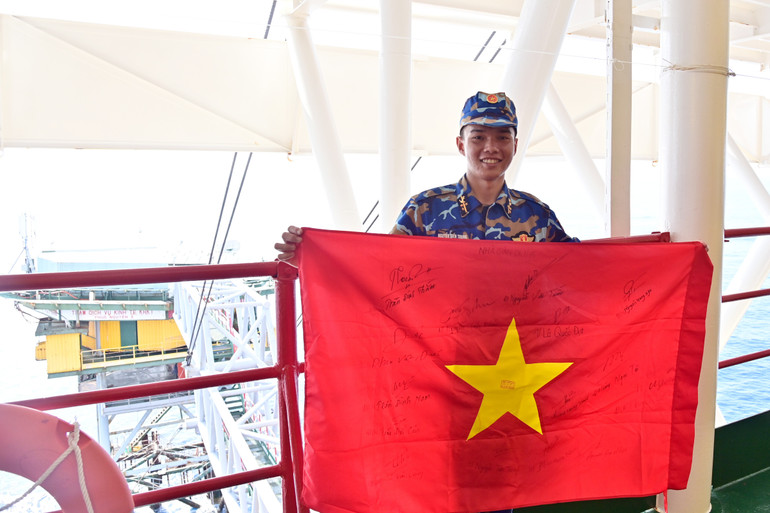 ពេលបញ្ចប់ភារកិច្ចនៅវេទិកា DK1/15 ពលបាលឯក ង្វៀន ទៀន ជុង បានយកទង់ជាតិមួយមកជាមួយ ដែលចុះហត្ថលេខាដោយនាយទាហាន និងទាហាននៃវេទិកា ជាវត្ថុអនុស្សាវរីយ៍។ 5-thuong-si-nguyen-tien-trung-chien-si-nha-gian-dk115-mang-theo-la-co-to-quoc-co-chu-ky-cua-can.jpg