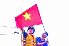 Cán bộ, chiến sĩ Đồn Biên phòng cửa khẩu cảng Thuận An tuyên truyền và tặng cờ Tổ quốc cho ngư dân vươn khơi, bám biển. (Ảnh VÕ TIẾN)