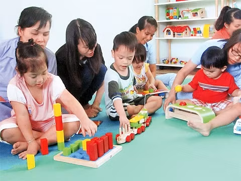 Giáo viên và tình nguyện viên hướng dẫn cho trẻ chơi bộ đồ chơi của mô hình tại Trung tâm NDBTTE Tam Bình.