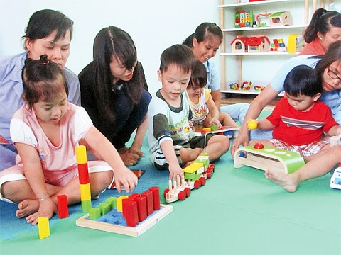 Giáo viên và tình nguyện viên hướng dẫn cho trẻ chơi bộ đồ chơi của mô hình tại Trung tâm NDBTTE Tam Bình.