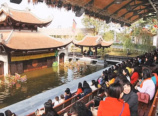 Du khách xem biểu diễn múa rối nước tại Làng văn hóa và ẩm thực Nắng Sông Hồng.