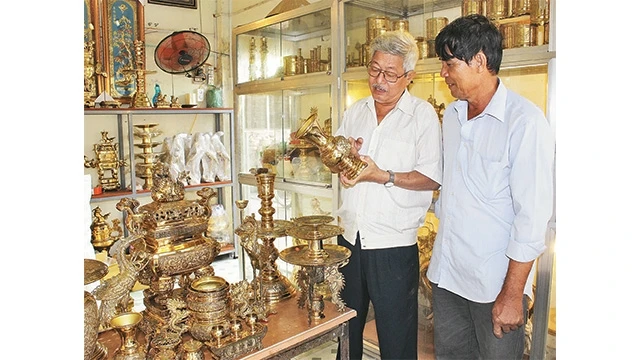 Ông Trần Văn Thắng (người bên trái) giới thiệu những hoa văn, họa tiết tinh xảo trên sản phẩm lư đồng với khách hàng.